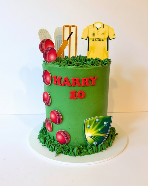 Green birthday cake with cricket-themed decorations, including red balls, a yellow Australia jersey, and a cricket bat, on a white background.