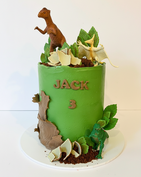 Green birthday cake with dinosaur figures 
