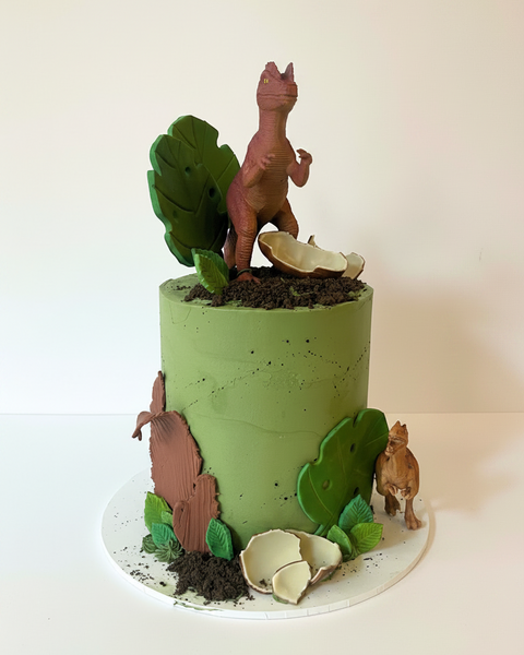 A decorated cake designed to look like a dinosaur-themed scene, with green icing and fondant dinosaurs on top.