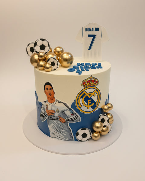 Cake with soccer-themed decorations, including a player illustration and sports balls, on a plain background.