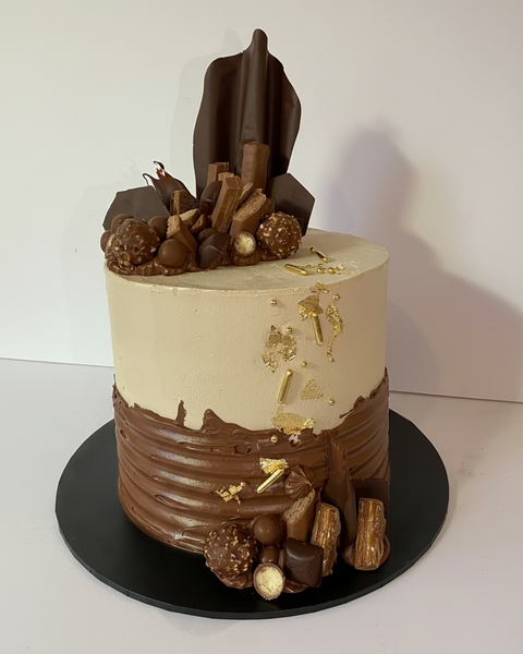  chocolate cake with a sail made from chocolate, gold decorations, and an assortment of chocolate treats on top.